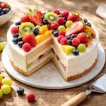 Friss gyümölcsökkel díszített, színes, házi készítésű gyümölcstorta egy fehér tányéron.